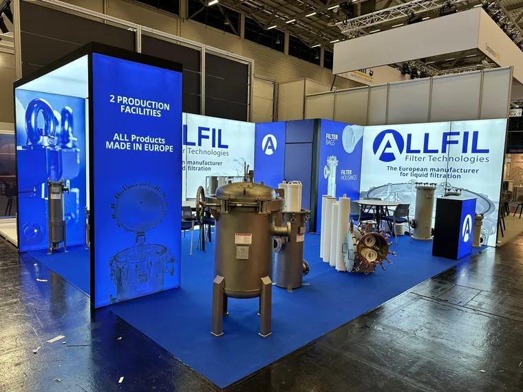Stoisko z podświetlanymi ścianami z logo Allfil i obudowami filtrów ustawionymi na niebieskiej wykładzinie