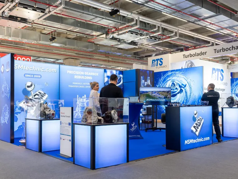 Stoisko półwyspowe z podświetlanymi ścianami i gablotami z przekładniami na targach Automechanika