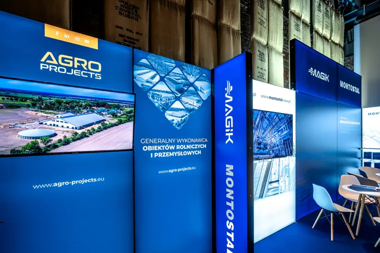 Wolnostojące ścianki z grafiką Agro Projects i telewizorem obok podświetlanej ściany