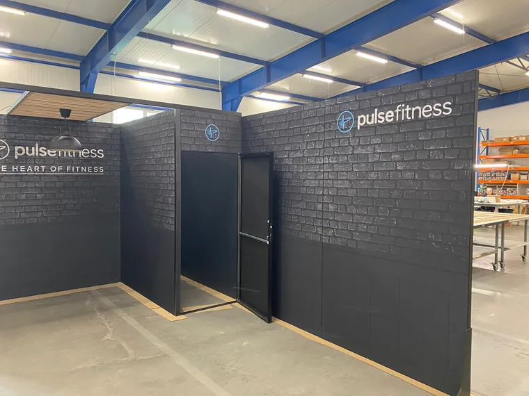 Ściany z grafiką ciemnej cegły i logo pulsefitness, ściana z drzwiami do zaplecza